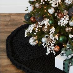 a christmas tree with presents under it on a black rug next to a white box