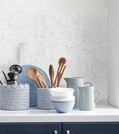 kitchen utensils and spoons are sitting on the countertop in front of a white hexagonal tile backsplash