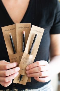 the woman is holding three small pencils in their hands and some brown paper bags