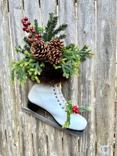 a pair of white ice skates with pine cones and berries on them sitting against a wooden fence