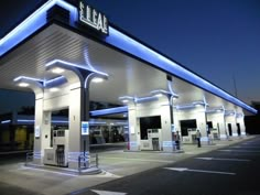 an empty gas station at night with blue lights on the front and white trimmings