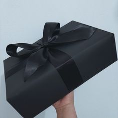 a hand holding a black gift box with a bow