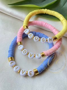 three bracelets with words on them sitting on top of a table next to a plant