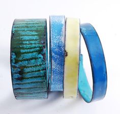 three different colored bracelets sitting next to each other on a white surface with blue and yellow bands around them