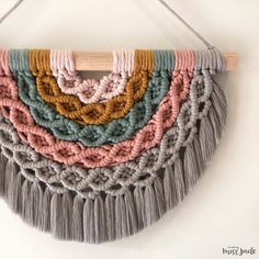 a multicolored macrame wall hanging on a white wall next to a wooden hanger