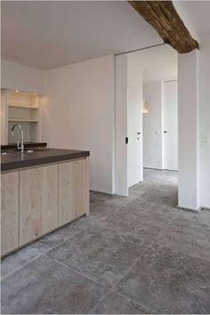 an empty kitchen and living room in a house with white walls, concrete flooring and exposed beams