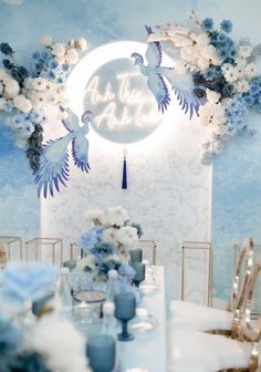 a blue and white table setting with flowers, candles and birds on the wall above it