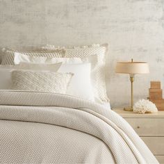 a bed with white linens and pillows in a neutral room next to a night stand