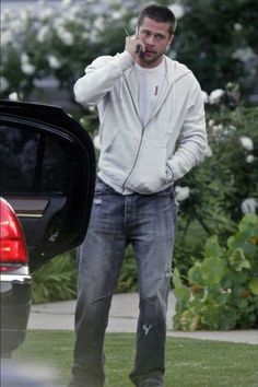 a man talking on a cell phone while standing next to a car in the grass