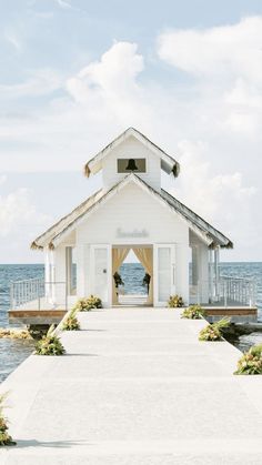 a small white house on the water with a gazebo and flowers in front of it