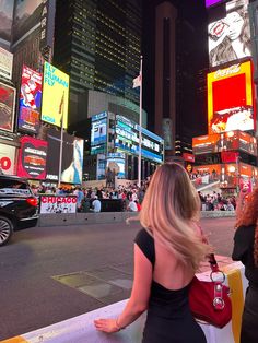 a woman in a black dress is sitting on a bench looking at the city lights