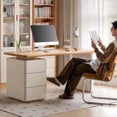 a man sitting at a desk reading a book in front of a computer monitor and keyboard