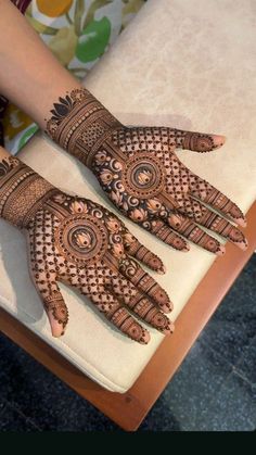 two hands with henna tattoos on them sitting on a table next to a chair