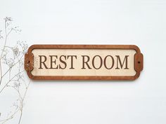 a wooden sign that says rest room on the side of a wall next to some flowers