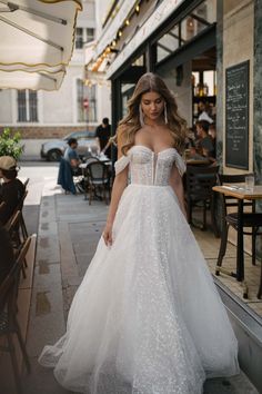 a woman is walking down the street in a wedding dress with an off shoulder design