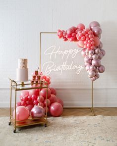 a birthday balloon arch with pink and silver balloons on it next to a cake stand