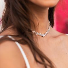 a woman wearing a white top with a diamond necklace on her neck, looking at the camera