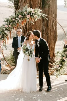 a bride and groom kissing in front of an outdoor wedding arch with flowers on it