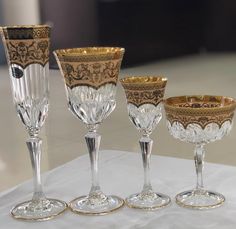 four glass goblets sitting on top of a white tableclothed table cloth