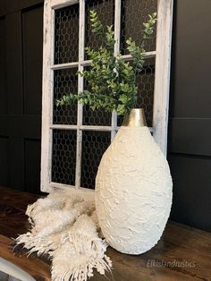 a white vase sitting on top of a wooden table next to an old window frame