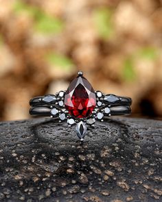 a close up of a ring with a red stone in the center on a rock