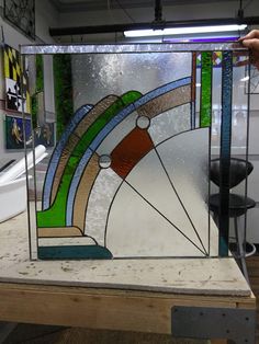 a person holding up a stained glass window in front of a mirror on a workbench