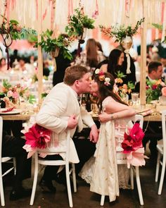 a bride and groom kissing in front of their guests at a dinner table decorated with flowers