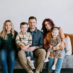 a family sitting on a couch in front of a white wall, smiling at the camera