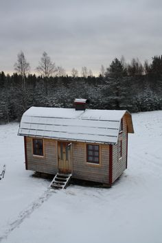 a small cabin sits in the middle of a snow - covered field with stairs leading up to it