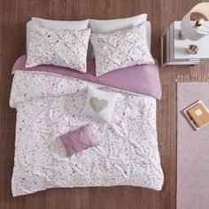 a bed with pink and white sheets on it next to a night stand, lamp and nightstand