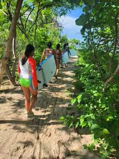 several people carrying surfboards down a dirt path