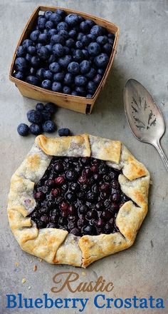 a blueberry crostaa pie sitting on top of a table next to a box of blueberries