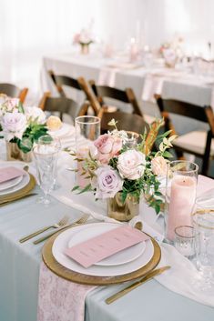 the table is set with pink and white flowers in vases, gold rimmed glasses, and place settings