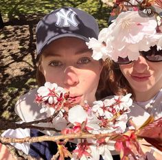 two girls wearing baseball caps and sunglasses are posing for the camera with flowers in front of them