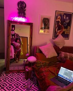 a laptop computer sitting on top of a couch in front of a pink neon sign