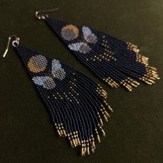 the beaded earrings are designed with blue beads and gold accents on black leather background