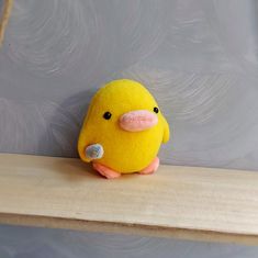 a small yellow bird sitting on top of a wooden shelf next to a gray wall