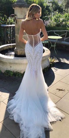 a woman in a wedding dress is standing near a fountain with her back to the camera