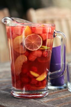 a pitcher filled with fruit sitting on top of a wooden table next to two glasses