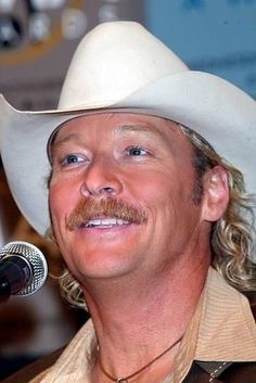 a man wearing a white cowboy hat with a microphone in front of him and smiling at the camera