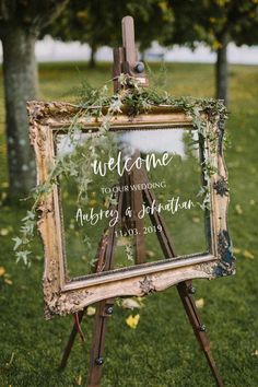 an easel with a sign that says welcome to the wedding and is decorated with greenery