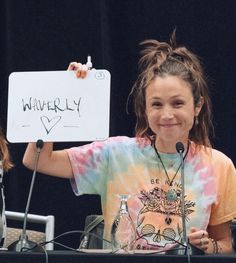 a woman holding up a sign in front of her at a podium with two microphones