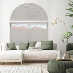 a living room with white furniture and green pillows on the couch, along with a large window