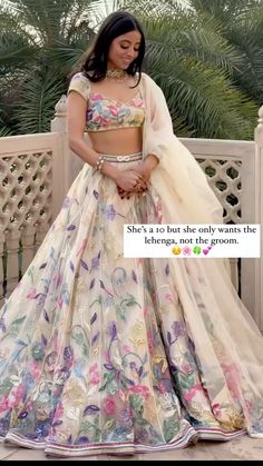 a woman in a white and pink lehenga standing on a balcony with palm trees