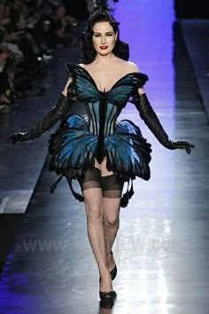 a woman walking down a runway wearing a blue butterfly dress and black gloves on her head