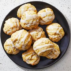 a black plate topped with frosted scones on top of a white countertop