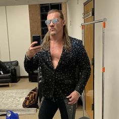 a man with long hair and sunglasses is taking a selfie in front of a mirror