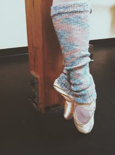 a woman's feet in ballet shoes next to a wooden post with her leg up