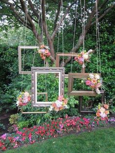 an outdoor area with flowers and frames hanging from the trees, in front of some bushes