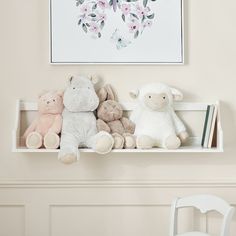 three stuffed animals are sitting on a shelf in front of a framed painting and chair